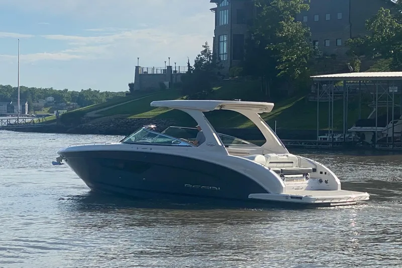 Slide: The Image of 2021 Regal 3300 Bowrider boat cruising on a scenic lake near a modern building. - 2