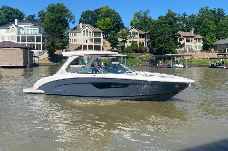 Slide: The Image of 2021 Regal 3300 Bowrider boat cruising on a scenic lake near a modern building. - 45