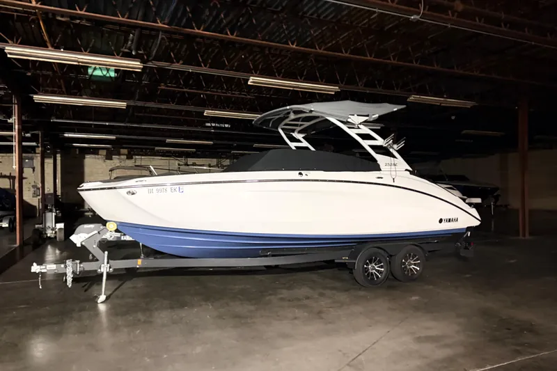 The Image of 2023 Yamaha Boats 252SE in a dimly lit indoor storage facility. - 0