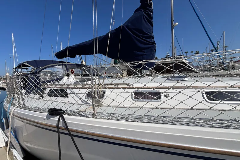 Slide: The Image of 1990 Catalina 42 sailboat docked, featuring netting and covered sails under clear blue sky. - 3