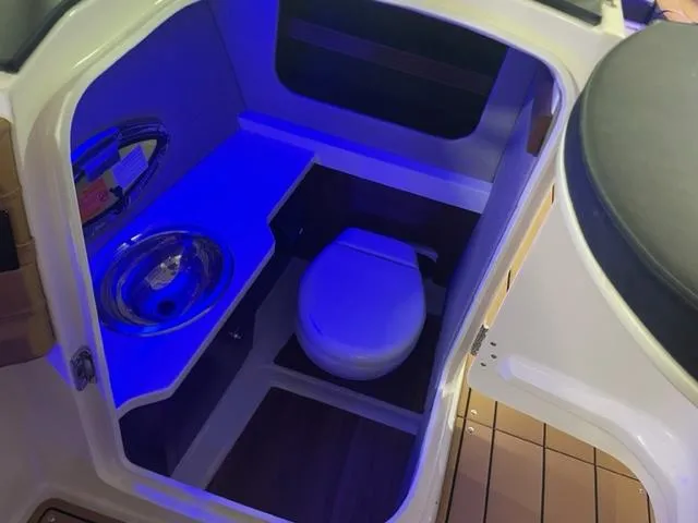 Slide: The Image of 2023 Chaparral 307 SSX boat bathroom with sink and toilet, blue ambient lighting. - 11