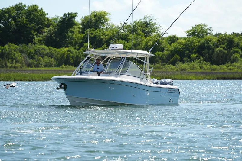 Slide: The Image of 2022 Grady-White Freedom 285 boat cruising on a sunny day near lush green shoreline. - 9