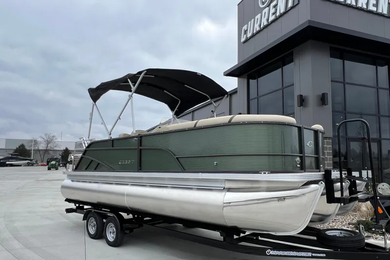 The Image of 2024 Crest Classic LX 220 SLRC pontoon boat on trailer outside dealership. - 0