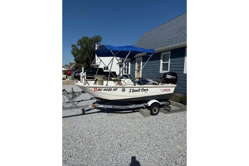 Slide: The Image of 2017 Boston Whaler 110 Sport boat with blue canopy on trailer, parked on gravel. - 9