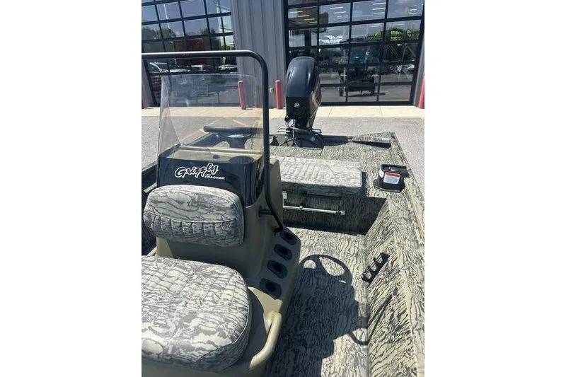Slide: The Image of 2026 Tracker Grizzly 1860 CC boat with camouflage seats and console, parked outdoors. - 12