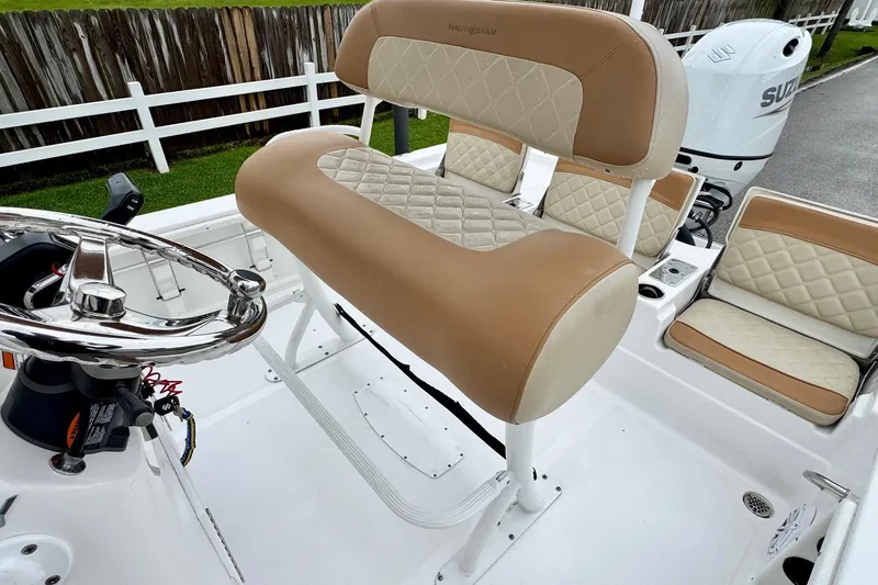 Slide: The Image of 2024 NauticStar 214 Bay boat interior with tan and white seating, steering wheel, and Suzuki engine. - 9