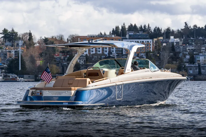 Slide: The Image of 2025 Chris-Craft Launch 35 GT cruising on a scenic lake with cityscape backdrop. - 2