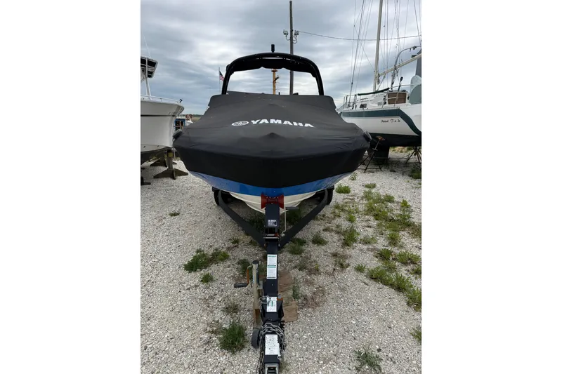 The Image of 2019 Yamaha AR210 boat with cover on trailer, parked on gravel lot. - 1