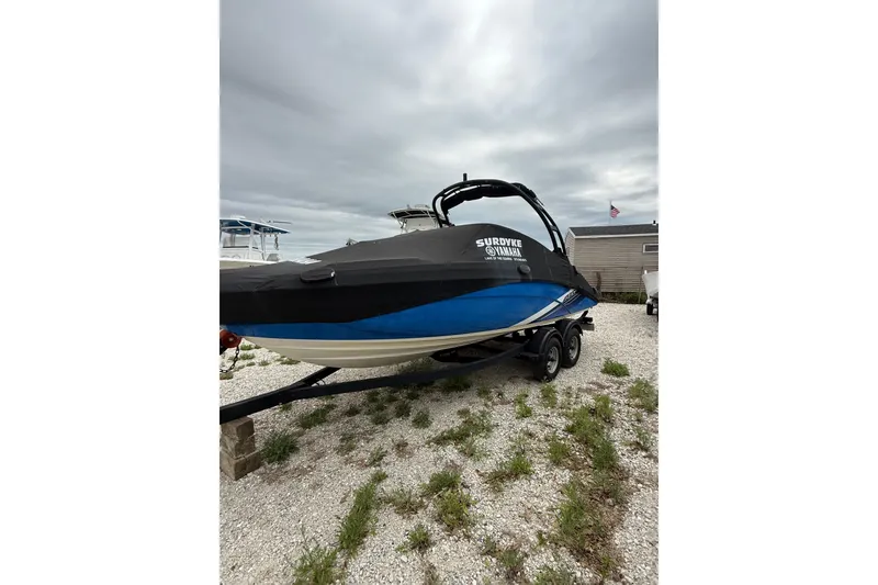 Slide: The Image of 2019 Yamaha AR210 boat with cover on trailer, parked on gravel lot. - 3