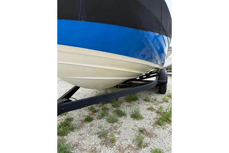 Slide: The Image of 2019 Yamaha Boats AR210 on trailer, blue and white hull, parked on gravel. - 5