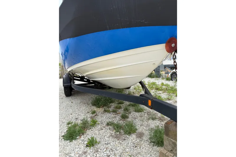 Slide: The Image of 2019 Yamaha Boats AR210 on trailer, blue and white hull, parked on gravel. - 6