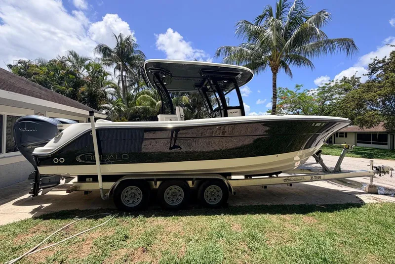 Slide: The Image of 2022 Robalo R302 Center Console boat on trailer, surrounded by palm trees. - 2