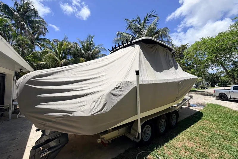 Slide: The Image of 2022 Robalo R302 Center Console boat covered on trailer, surrounded by palm trees. - 4