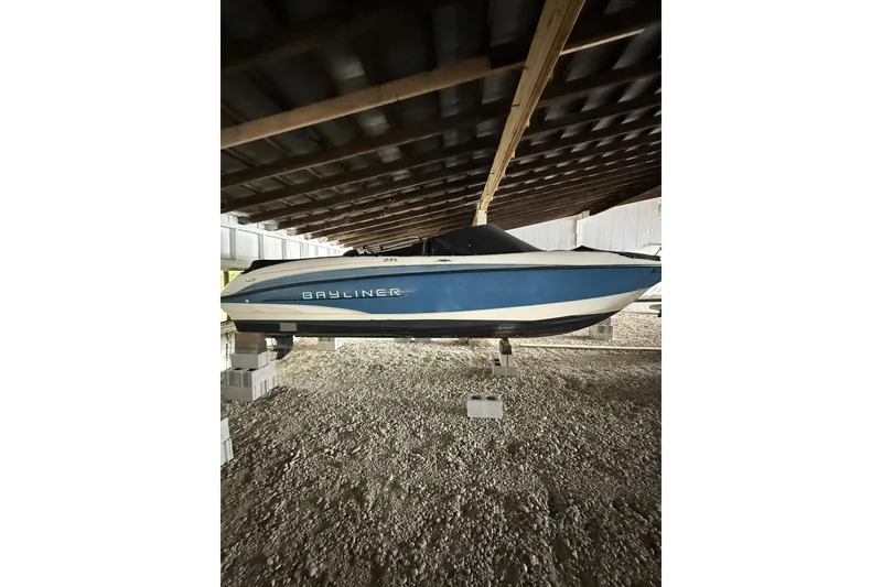 Slide: The Image of 2012 Bayliner 235 Bowrider boat stored under a covered structure on blocks. - 3