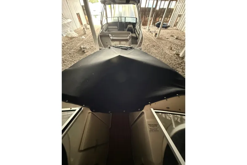 Slide: The Image of 2012 Bayliner 235 Bowrider with cover, stored indoors on gravel surface. - 35