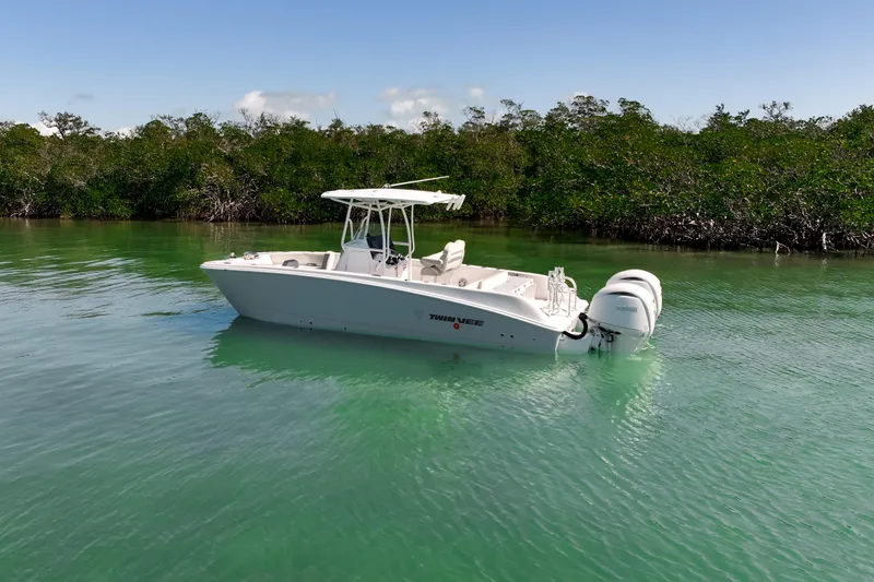 Slide: The Image of 2026 Twin Vee 240 GFX CC boat on calm water, surrounded by lush greenery. - 34