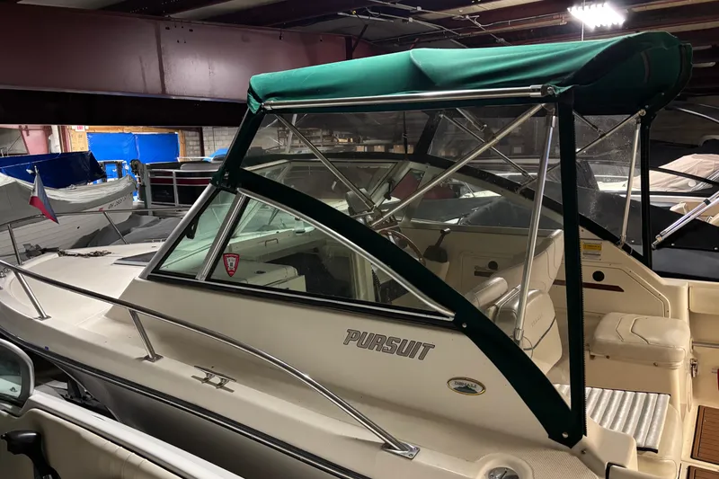 The Image of 1999 Pursuit 2460 Denali boat with green canopy in indoor storage. - 0