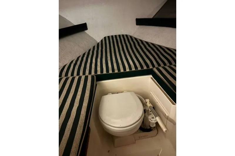 Slide: The Image of 1999 Pursuit 2460 Denali boat interior with striped cushions and compact toilet. - 7