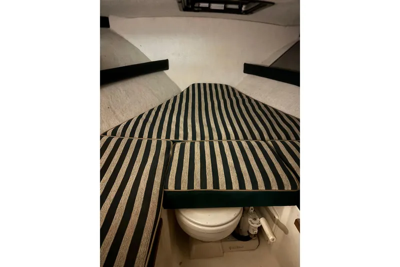 Slide: The Image of 1999 Pursuit 2460 Denali cabin interior with striped cushions and compact toilet. - 8