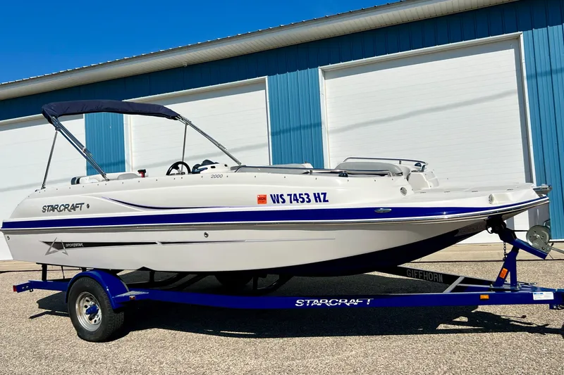 The Image of 2014 Starcraft 2000 IO Limited boat on trailer, parked outside blue building. - 0