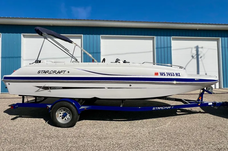 Slide: The Image of 2014 Starcraft 2000 IO Limited boat on trailer, parked outside blue building. - 2