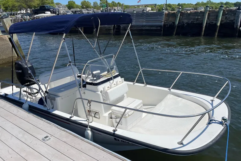 The Image of 2009 Boston Whaler 150 Montauk boat docked, featuring a blue canopy and Mercury outboard motor. - 0