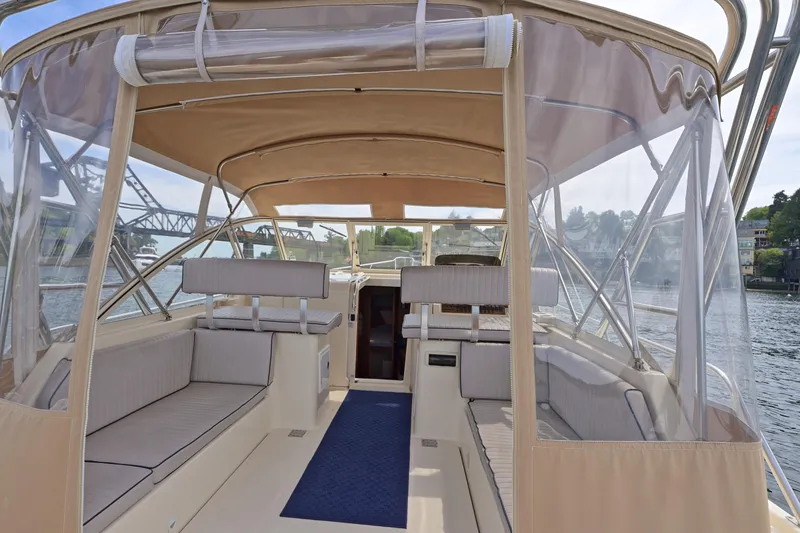 Slide: The Image of 2004 Mainship Pilot 34 boat interior with beige seating and clear canopy on a calm waterway. - 16