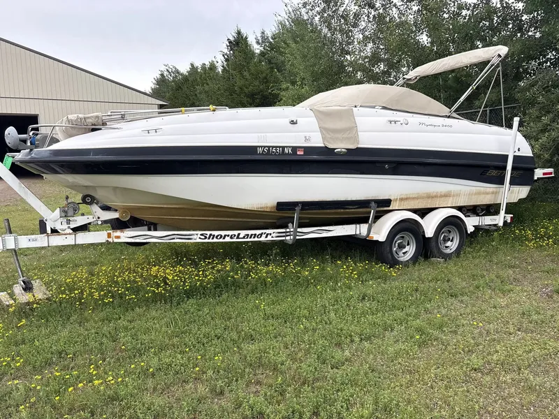 The Image of A 2000 Ebbtide MYST 2400FUN/DC boat on a trailer, surrounded by grass and trees. - 1