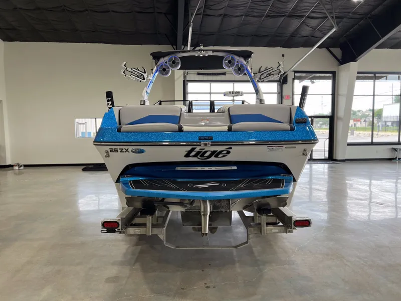 Slide: The Image of Rear view of a blue 2021 Tigé 25ZX boat in a showroom. - 4