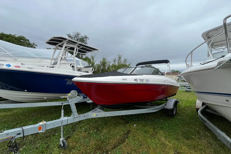 Slide: The Image of 2024 Bayliner VR4 Bowrider OB on trailer, parked between boats, overcast sky. - 2