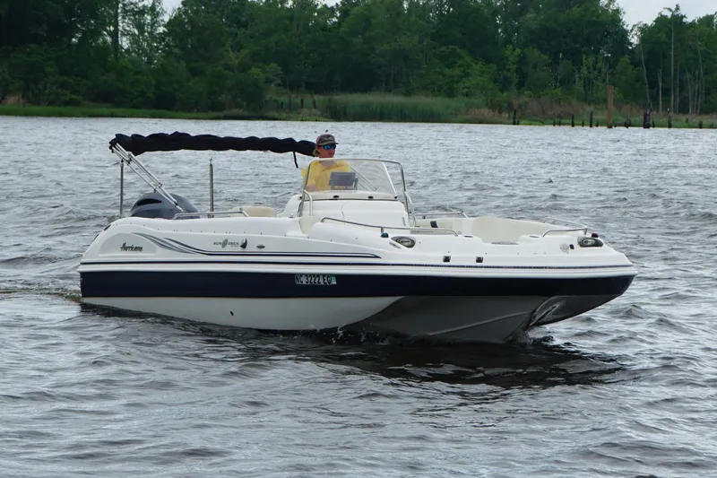 The Image of 2015 Hurricane SunDeck Sport 231 OB boat cruising on a lake with trees in the background. - 0