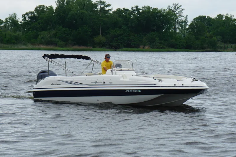 Slide: The Image of 2015 Hurricane SunDeck Sport 231 OB boat cruising on a lake with lush green background. - 17