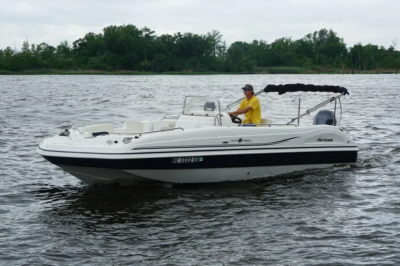 Slide: The Image of 2015 Hurricane SunDeck Sport 231 OB boat cruising on a calm lake with a driver. - 2