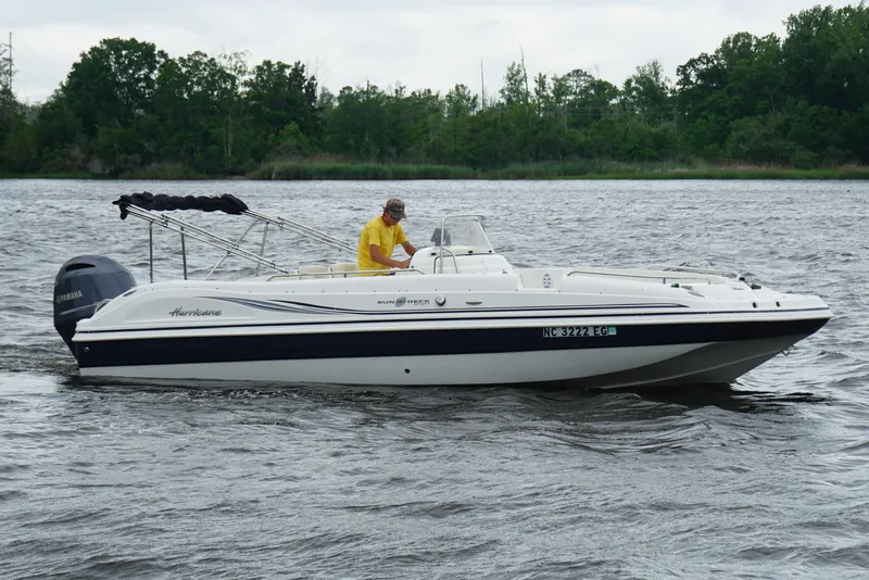 Slide: The Image of 2015 Hurricane SunDeck Sport 231 OB boat cruising on a lake with lush green trees. - 23