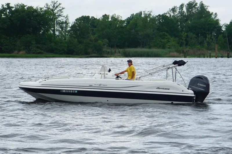 Slide: The Image of 2015 Hurricane SunDeck Sport 231 OB boat on water, person steering, lush green background. - 3