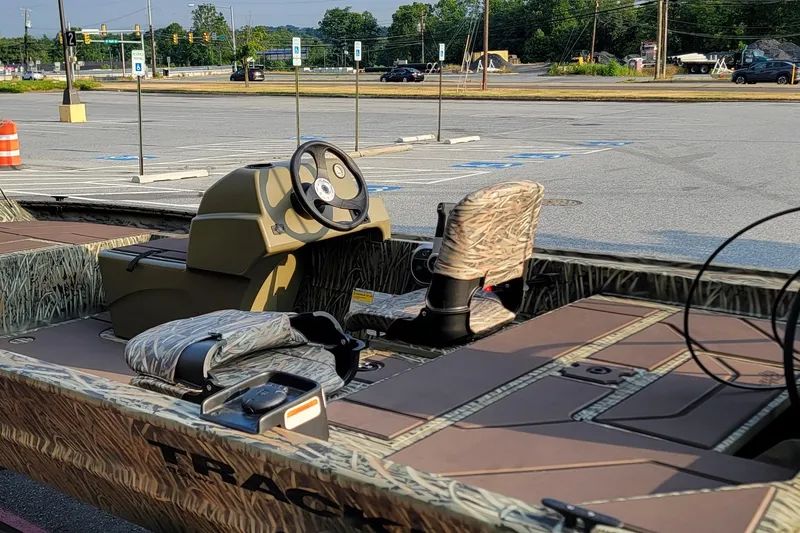 Slide: The Image of 2026 Tracker Grizzly 1754 SC boat interior with camouflage seating in a parking lot. - 2