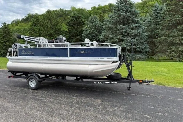 Slide: The Image of 2026 Sun Tracker Bass Buggy 18 DLX pontoon boat on trailer, parked on paved road. - 2