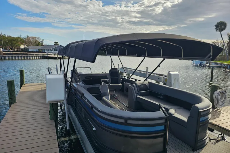 Slide: The Image of 2024 Harris pontoon boat docked by a serene waterfront under a cloudy sky. - 3