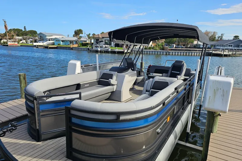 Slide: The Image of 2024 Harris pontoon boat docked by waterfront homes under a clear blue sky. - 5