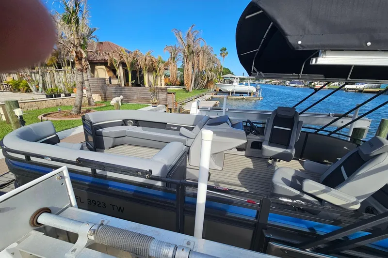 Slide: The Image of 2024 Harris pontoon boat with gray seating, docked by a waterfront home. - 6