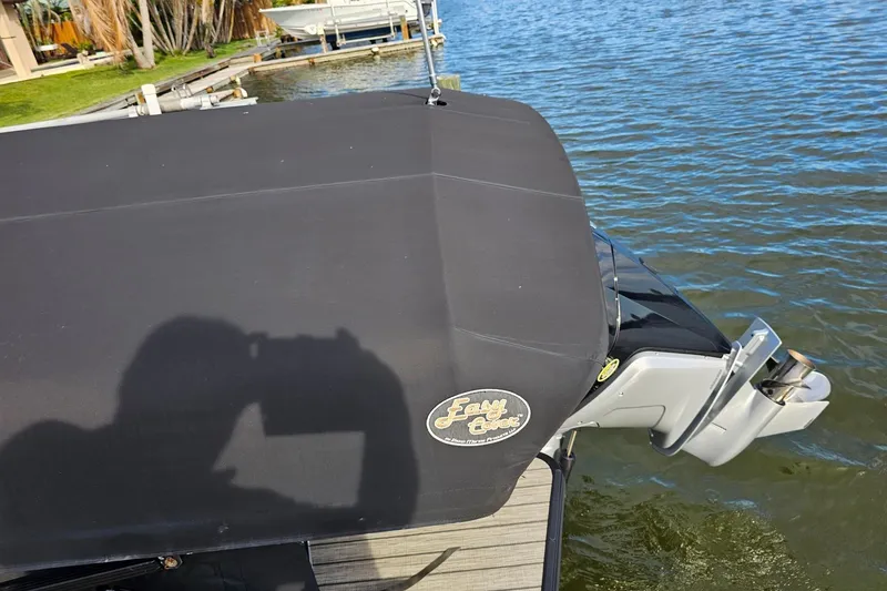 Slide: The Image of 2024 Harris boat with black cover docked by a lake, featuring an outboard motor. - 8