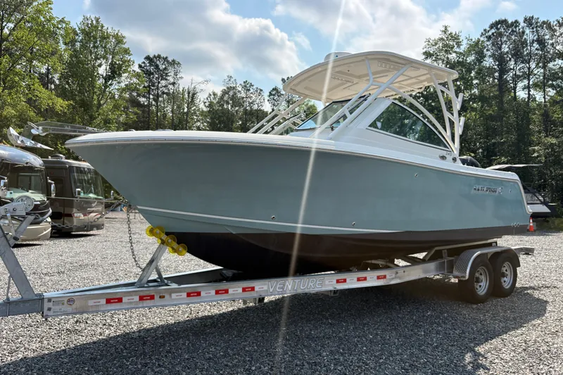 Slide: The Image of 2017 Sailfish 245 DC boat on trailer, parked outdoors with trees in background. - 25