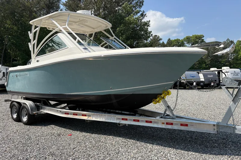 Slide: The Image of 2017 Sailfish 245 DC boat on trailer, parked outdoors, surrounded by trees and RVs. - 28