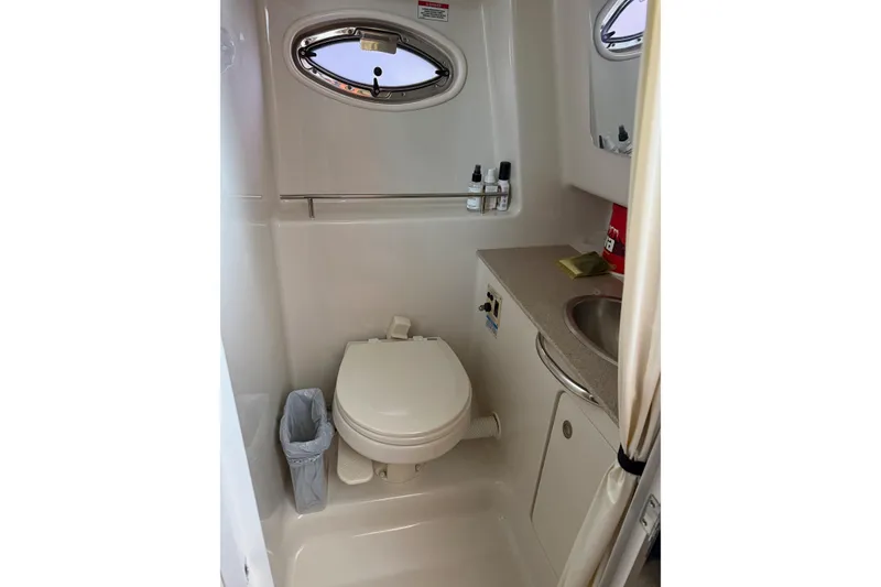 Slide: The Image of Compact bathroom in 2007 Sea Ray 290 Sundancer boat, featuring toilet, sink, and porthole window. - 15