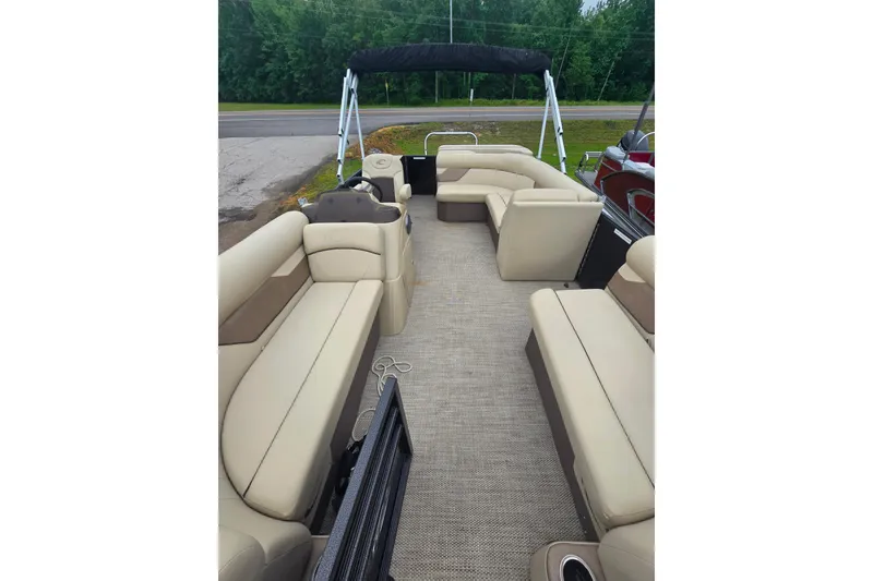 Slide: The Image of 2019 Crest I L Cp2 pontoon boat interior with beige seating and canopy, parked near greenery. - 8