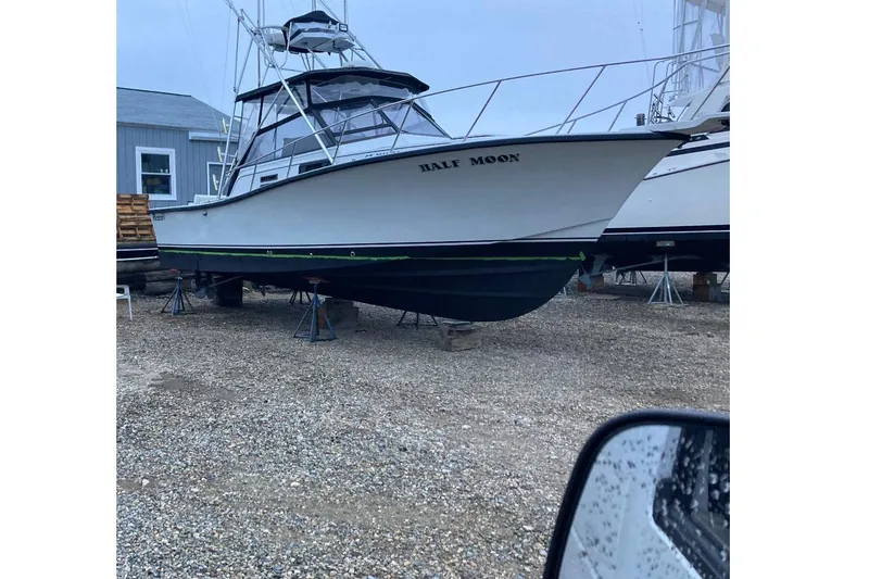 Slide: The Image of 1988 Rampage 31 Express boat named "Half Moon" on dry dock, gravel ground. - 3