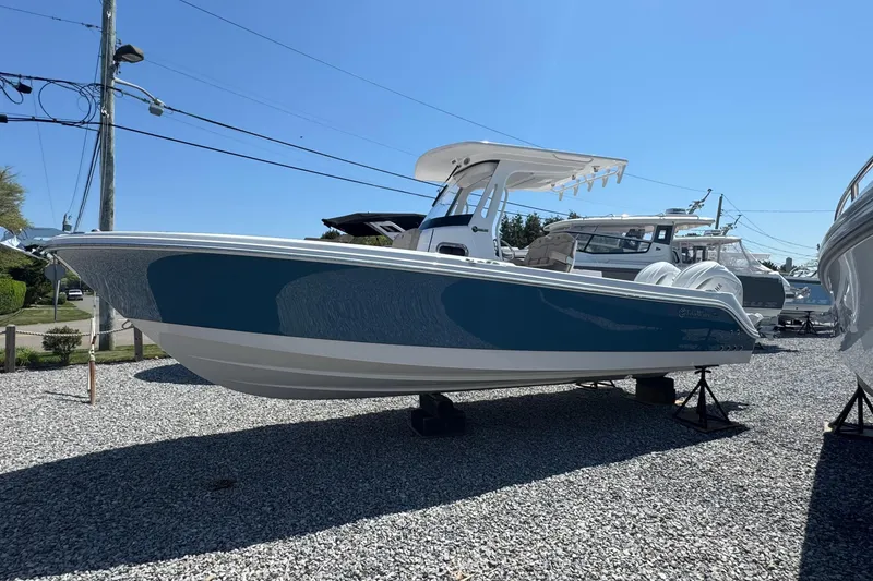 Slide: The Image of 2026 Edgewater 262CC boat displayed outdoors on gravel lot under clear blue sky. - 2