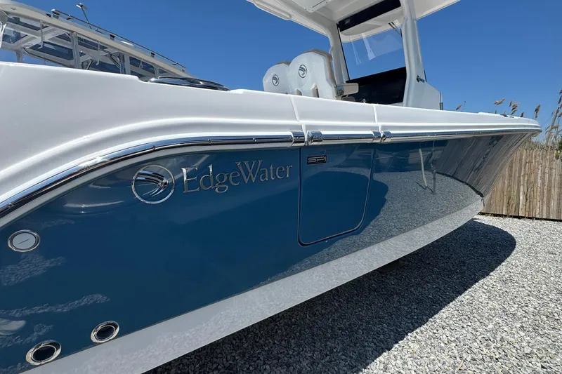 Slide: The Image of 2026 Edgewater 262CC boat with sleek blue and white design, parked on gravel. - 4