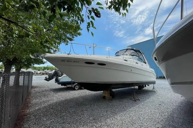 The Image of 2000 Sea Ray 340 Sundancer yacht on gravel lot, surrounded by trees and boats. - 0