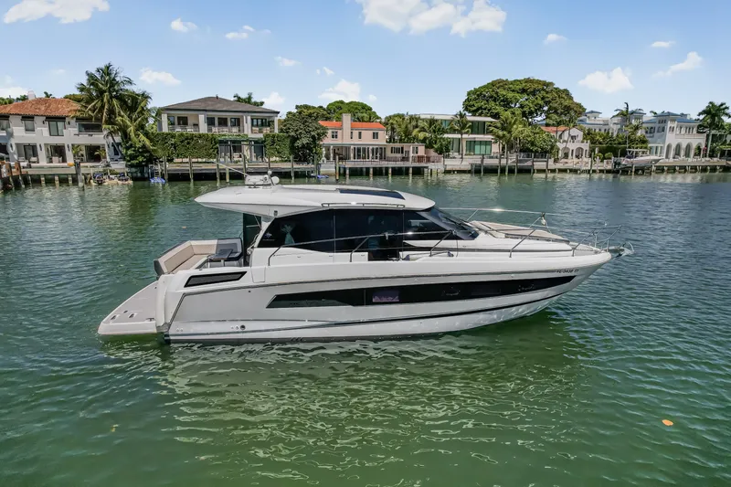 Slide: The Image of 2020 Jeanneau NC 37 yacht cruising on a scenic waterfront with luxury homes. - 2